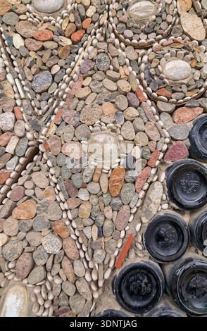 Textured external wall of the Bottle House in Ganja, Azerbaijan, featuring a mosaic of colorful stones, white pebbles, and dark glass bottle bottoms Stock Photo