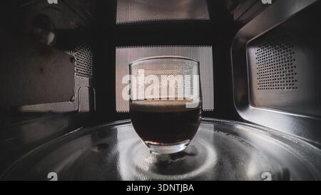 Cup of coffee heating inside microwave oven, interior view of kitchen appliance Stock Photo