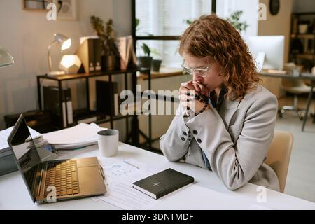 Young Woman Praying at Desk While Working in Business Office Stock Photo