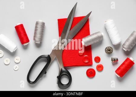 Thread spools with scissors, buttons, fabric and thimble on grey background Stock Photo