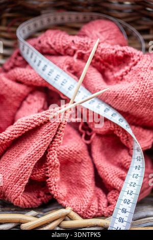 Close up photo of a knitting project in a basket with soft yarn wooden needles and a measuring tape The scene shows handmade work craft materials and Stock Photo
