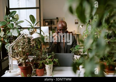 Black Man Working on Laptop and Talking on Smartphone in Office Stock Photo