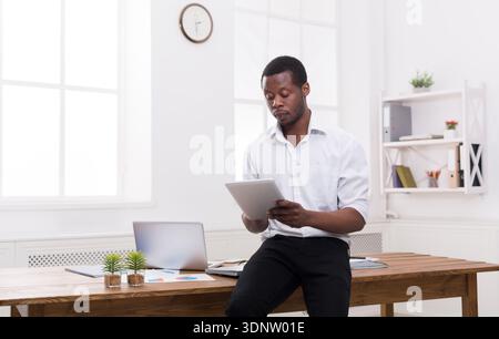 Serious black businessman in modern office, work with tablet Stock Photo