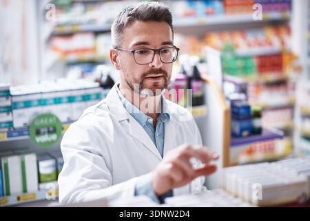 Mature man, pharmacist or checking inventory with shelf in dispensary for self service medication. Male person, chemist or doctor counting stock in Stock Photo