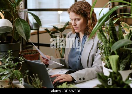 Young Woman Analyzing Documents While Working on Laptop Stock Photo