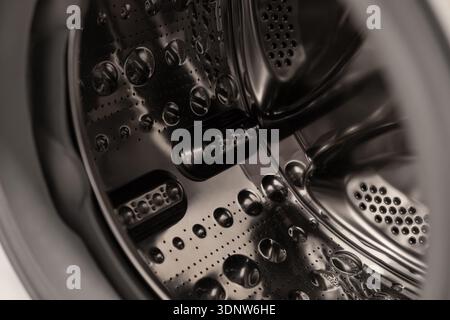 Top-down view of a clean empty modern washing machine drum, featuring shiny perforated stainless steel and textured elements, symbolizing household cl Stock Photo