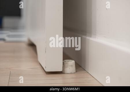 Detailed close-up view of a durable concrete door stop effectively holding a pristine white wooden interior door ajar on a light laminate floor, provi Stock Photo