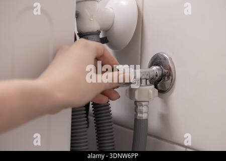 Close-up of a female hand turning a metal valve for water supply control to a household appliance, representing essential home plumbing work and DIY r Stock Photo