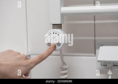 Close-up of a hand setting temperature levels on a stylish electronic control unit of a wall-mounted towel warmer, promoting domestic well-being and c Stock Photo