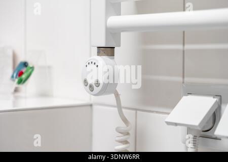 Detailed view of a white electric towel warmer, highlighting its digital control panel and coiled power cable, representing a modern, practical bathro Stock Photo