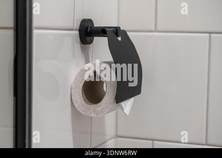 Close-up of a recycled toilet paper roll securely held by a sleek black dispenser, highlighting contemporary bathroom design and personal care necessi Stock Photo