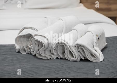 Krakow, Poland - November 30, 2025: Soft white rolled towels elegantly presented on a gray quilted bedspread, highlighting premium hotel amenities, gu Stock Photo