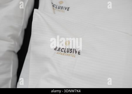 Krakow, Poland - November 30, 2025: Close-up of EXCLUSIVE APARTHOTEL brand, golden emblem on fresh white striped bedding, showcasing quality, hygiene, Stock Photo