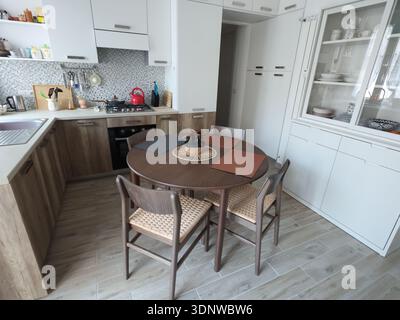 Living room design combined with kitchen, featuring white sideboard. Set of wooden furniture with beech veneer, table, and chairs. Scandinavian-style Stock Photo