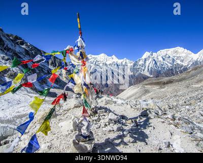 A scene from the Himalayan mountains in Nepal, featuring traditional Tibetan prayer flags in the foreground against a backdrop of snow-covered peaks Stock Photo