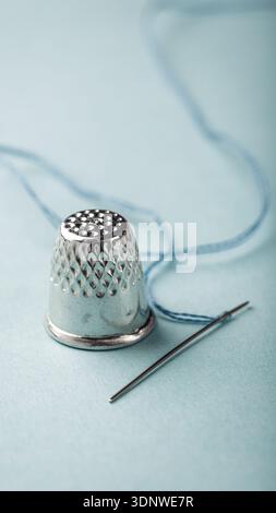 Silver thimble and needle with blue thread on soft pastel background for sewing enthusiasts Stock Photo