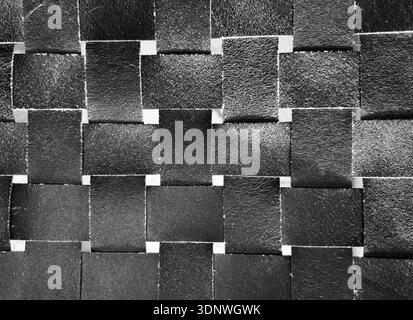 Woven black leather squares create geometric textured surface. Interlaced matte strips form seamless background pattern. Stock Photo