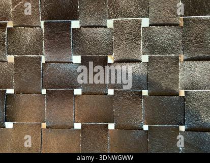 Woven leather squares form geometric grid texture. Interlaced dark strips create seamless background surface. Stock Photo