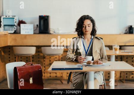 Businesswoman having coffee break with croissant at cafe Stock Photo