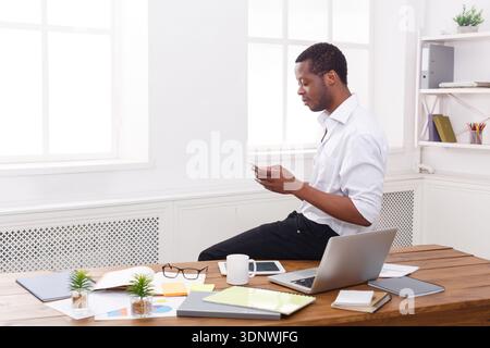 Young black businessman with mobile in modern white office Stock Photo