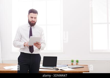 Young concentrated businessman in white shirt and tie standing and reading documents Stock Photo