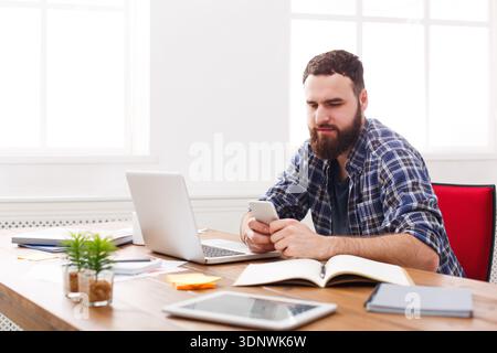 Young IT manager in office using cell phone by the laptop Stock Photo