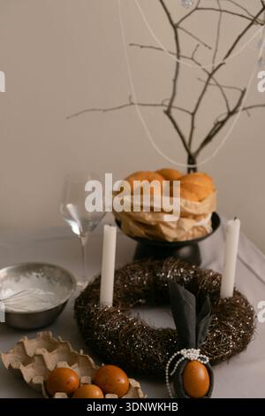 On festive Easter table, cake decorated with white icing, with eggs in tray, candles, and twig wreath nearby. Stock Photo