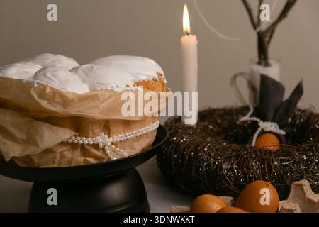 Easter composition with cake in white icing, colorful eggs, and candles in a twig nest on a festive holiday table. Stock Photo