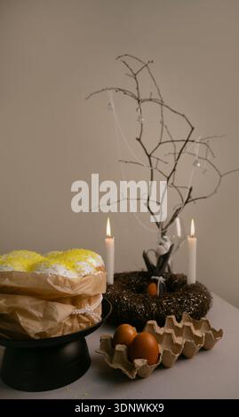 Cozy Easter composition with cake in white icing, colorful eggs in tray, candles, and twig wreath creating festive atmosphere. Stock Photo