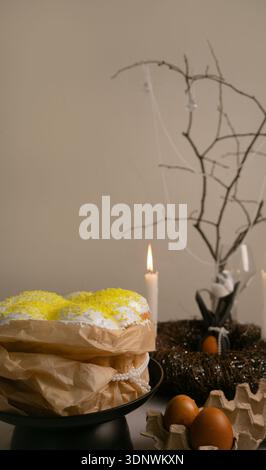 Festive Easter table with cake in white icing, painted eggs, candles, and a neat twig nest centerpiece. Stock Photo