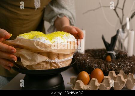 In home clothes, she arranges Easter cakes and colorful eggs on the table, preparing it with love and warmth. Stock Photo