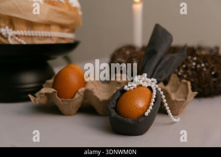 In foreground, Easter egg decorated with napkin bunny ears, festive table decoration for Easter evening celebration. Stock Photo