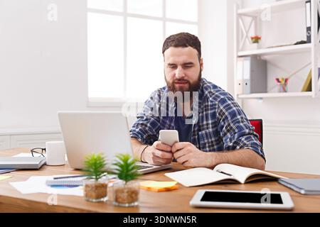 Young businessman in office using cell phone by the laptop Stock Photo