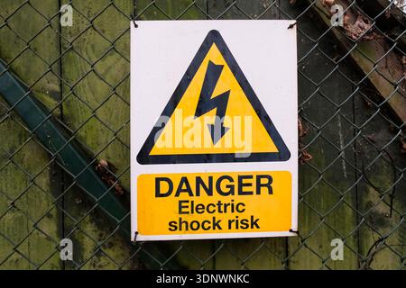 Danger electric shock risk warning sign attached to fence. United Kingdom Stock Photo