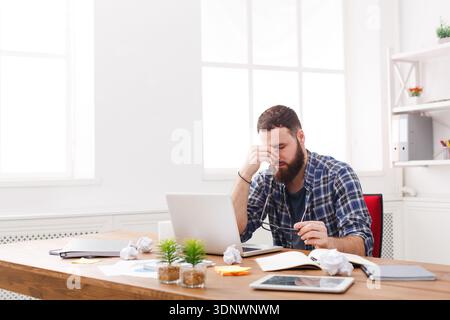 Tired, overworking businessman with laptop in modern white office Stock Photo