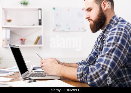 Young businessman in office using cell phone by the laptop Stock Photo