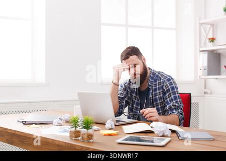 Tired stressed male programmer with laptop in modern white office Stock Photo