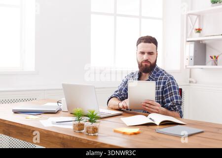 Young concentrated man using tablet at the table with laptop Stock Photo