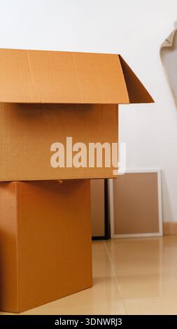 Moving boxes stacked in a room with blank frames on the floor during daytime Stock Photo