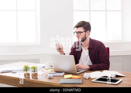 Thoughtful young businessman looking on smartphone in modern white office Stock Photo