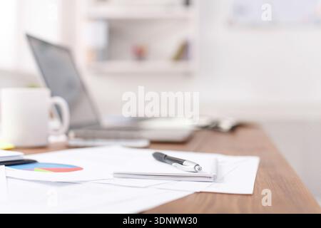 Side view of office desk with pen on the notebook, laptop and other items Stock Photo
