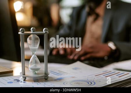 Middle Aged Black Man Working on Laptop with Hourglass in Office Setting Stock Photo