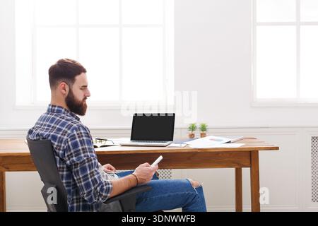 Young successful beard businessman with laptop and mobile phone in modern white office Stock Photo