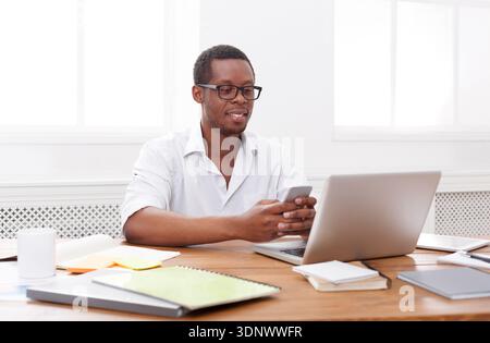 Happy black businessman in office at workplace with mobile Stock Photo
