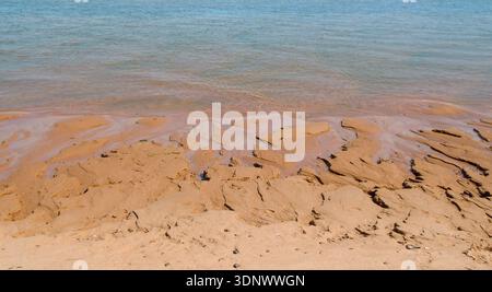 Intricate natural patterns in wet sand formed by receding water along a coastal shoreline, with branching channels creating an abstract texture. Stock Photo