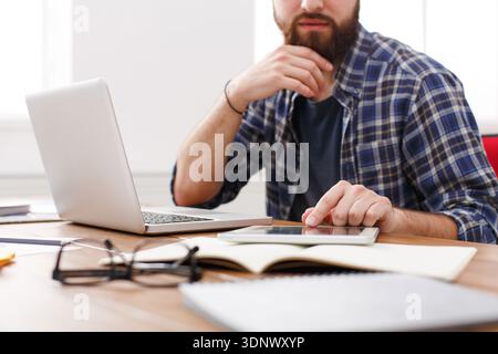 Close up of a serious man office worker is reading report, while is sitting at the table with open net-book. Stock Photo