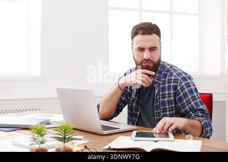 Close up portrait of a pensive young businessman sitting and using tablet computer in office Stock Photo