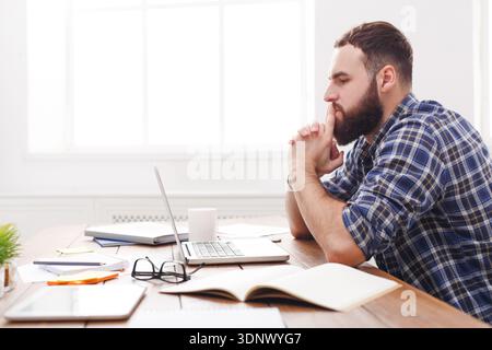 Young stressed man with laptop in modern white office from the side Stock Photo