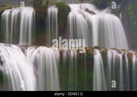 The main curtains of Ban Gioc Waterfall flow over tiered limestone cliffs in smooth, vertical streams. Stock Photo