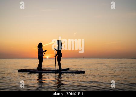 Couple of tourists young man and woman having fun paddle boarding at sea Stock Photo